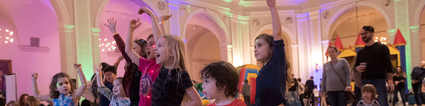 Children cheering, laughing, and waving their hands in a large, colorfully lit space during Family Day Benefit 2018