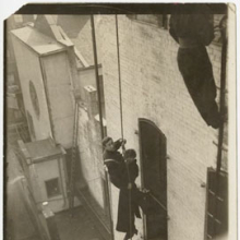 Djuna Barnes and unidentified fireman, dangling from a rope beside a building