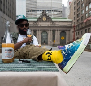 <p>Marquis Williams sits outdoors on Park Avenue, with Grand Central Terminal in the background, holding a glass of wine and with their foot on a table.</p>