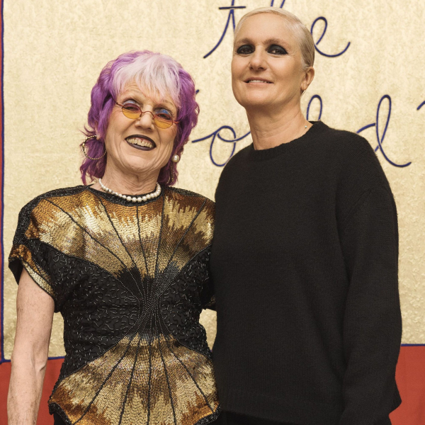 <p>Judy Chicago and Maria Grazia Chiuri stand next to each other, smiling, in front of a colorful banner. They are shown from the knees up.</p>