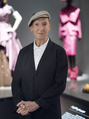 <p>Stephen Jones stands in a gallery, with two Christian Dior outfits on mannequins in the background.</p>