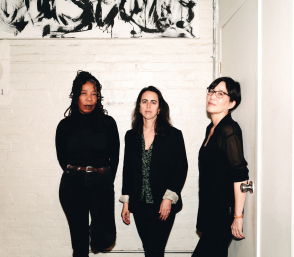 Three jazz musicians standing against a white brick wall