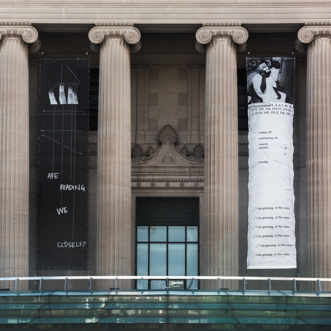 Straight on view of the front of the Museum showing only Kameelah Janan Rasheed's four banners from her exhibition Are We Reading Closely?, displayed among the building columns