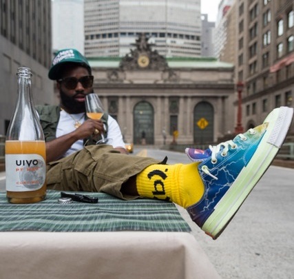 <p>Marquis Williams sits outdoors on Park Avenue, with Grand Central Terminal in the background, holding a glass of wine and with their foot on a table.</p>