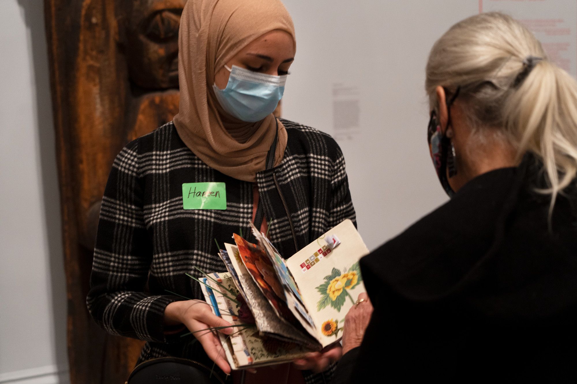 <p>A participant in a Museum program shows their book project to another person.</p>