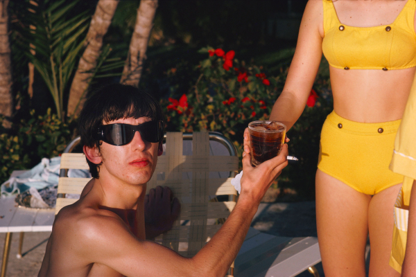 George Harrison taking a drink from a woman in a bikini