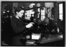 [Untitled]  (Young Woman Standing at Tabletop Thread Machine)