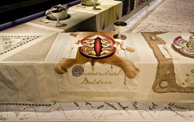 Judy Chicago (American, born 1939). <em>Primordial Goddess Place Setting</em>, 1974-1979. Runner:Cotton/linen base fabric, woven interface support material (horsehair, wool, and linen), cotton twill tape, silk, synthetic gold cord, unborn calf skins, cowry shells, stone beads, fabric paint, thread
Plate: Porcelain with overglaze enamel (China paint), Runner: 53 1/2 x 30 1/2 in. (135.9 x 77.5 cm). Brooklyn Museum, Gift of The Elizabeth A. Sackler Foundation, 2002.10-PS-1. © artist or artist's estate (Photo: , 2002.10-PS-01_Primordial_Goddess_Jook_Leung_photo_9284r2.jpg)