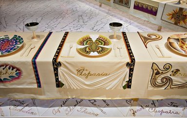 Judy Chicago (American, born 1939). <em>Aspasia Place Setting</em>, 1974-1979. Runner: Cotton/linen base fabric, woven interface support material (horsehair, wool, and linen), cotton twill tape, silk, stiffened cotton/linen fabric, “polished cotton” fabric, silk thread, metallic cord, cotton, thread
Plate: Porcelain with overglaze enamel (China paint), Runner: 52 x 30 in. (132.1 x 76.2 cm). Brooklyn Museum, Gift of The Elizabeth A. Sackler Foundation, 2002.10-PS-11. © artist or artist's estate (Photo: , 2002.10-PS-11_Aspasia_Jook_Leung_photo_9304r2.jpg)