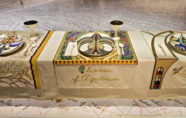 Judy Chicago (American, born 1939). <em>Eleanor of Aquitaine Place Setting</em>, 1974-1979. Runner: Cotton/linen base fabric, woven interface support material (horsehair, wool, and linen), cotton twill tape, silk, synthetic gold cord, tapestry, bleached linen, wool, silk satin, silk thread, felt, appliquéd fabric, thread
Plate: Porcelain with overglaze enamel (China paint) and rainbow luster glaze, Runner: 52 3/8 x 30 5/8 in. (133 x 77.8 cm). Brooklyn Museum, Gift of The Elizabeth A. Sackler Foundation, 2002.10-PS-19. © artist or artist's estate (Photo: , 2002.10-PS-19_Eleanor_of_Aquitaine_Jook_Leung_photo_9330r2.jpg)