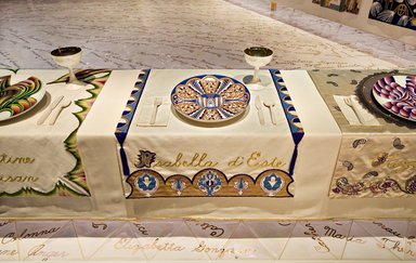 Judy Chicago (American, born 1939). <em>Isabella d'Este Place Setting</em>, 1974-1979. Runner: Cotton/linen base fabric, woven interface support material (horsehair, wool, and linen), cotton twill tape, silk, synthetic gold cord, thread, silk satin fabric, silk thread, cotton canvas, silk cord, handmade silk tassels
Plate: Porcelain with overglaze enamel (China paint), yellow luster, and rainbow overglaze, Runner: 52 1/8 x 30 3/8 in. (132.4 x 77.2 cm). Brooklyn Museum, Gift of The Elizabeth A. Sackler Foundation, 2002.10-PS-23. © artist or artist's estate (Photo: , 2002.10-PS-23_Isabella_dEste_Jook_Leung_photo_9338r2.jpg)