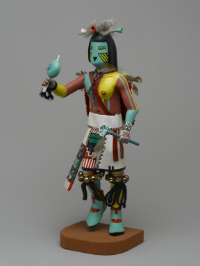 Henry Shelton (1929–2016). <em>Kachina Doll (Powaung Katsina)</em>, 1960–1970. Cottonwood root, acrylic paint, yarn,metal bells, feathers, leather, cotton, 14 1/2 × 5 × 6 1/2 in. (36.8 × 12.7 × 16.5 cm). Brooklyn Museum, Gift of Edith and Hershel Samuels, 2010.6.12. Creative Commons-BY (Photo: Brooklyn Museum, 2010.6.12_front_PS2.jpg)