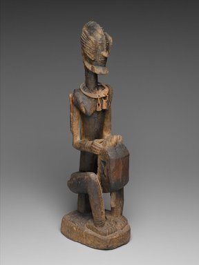 Dogon. <em>Figure of a Seated Musician (Koro Player)</em>, late 18th century. Wood, iron, 22 x 7 x 4 1/4 in. (55.8 x 17.7 x 10.8 cm). Brooklyn Museum, Frank L. Babbott Fund, 61.2. Creative Commons-BY (Photo: Brooklyn Museum, 61.2_threequarter_PS2.jpg)