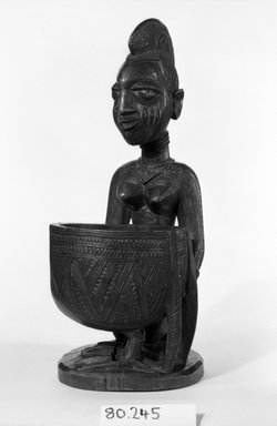 Yorùbá. <em>Kneeling Female Figure Holding a Bowl (Agere Ifa)</em>, late 19th or early 20th century. Wood, applied materials, (metal & beads in bag), h: 11 3/3 in. (30.0 cm). Brooklyn Museum, Gift of Ann W. Walzer, 80.245. Creative Commons-BY (Photo: Brooklyn Museum, 80.245_threequarter_bw.jpg)
