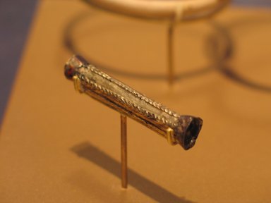  <em>Cylindrical Tube Amulet</em>, ca. 1938-1700 B.C.E. Gold, bronze, garnet, 3/16 x 1 9/16 in. (0.5 x 3.9 cm). Brooklyn Museum, Gift of the Egypt Exploration Fund, 13.1038. Creative Commons-BY (Photo: Brooklyn Museum, CUR.13.1038_erg2.jpg)