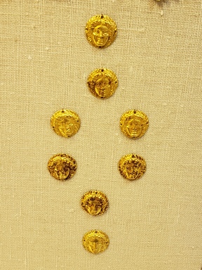 Greek. <em>Applique, Circular in Shape, with Female Face</em>, late 4th century B.C.E. Gold, 1/8 x 5/8 in. (0.3 x 1.6 cm). Brooklyn Museum, Gift of Mr. and Mrs. Thomas S. Brush, 71.79.175. Creative Commons-BY (Photo: Brooklyn Museum, CUR.71.79.172-.179_overall.jpg)