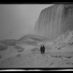 Two Men Standing at Base of Waterfall