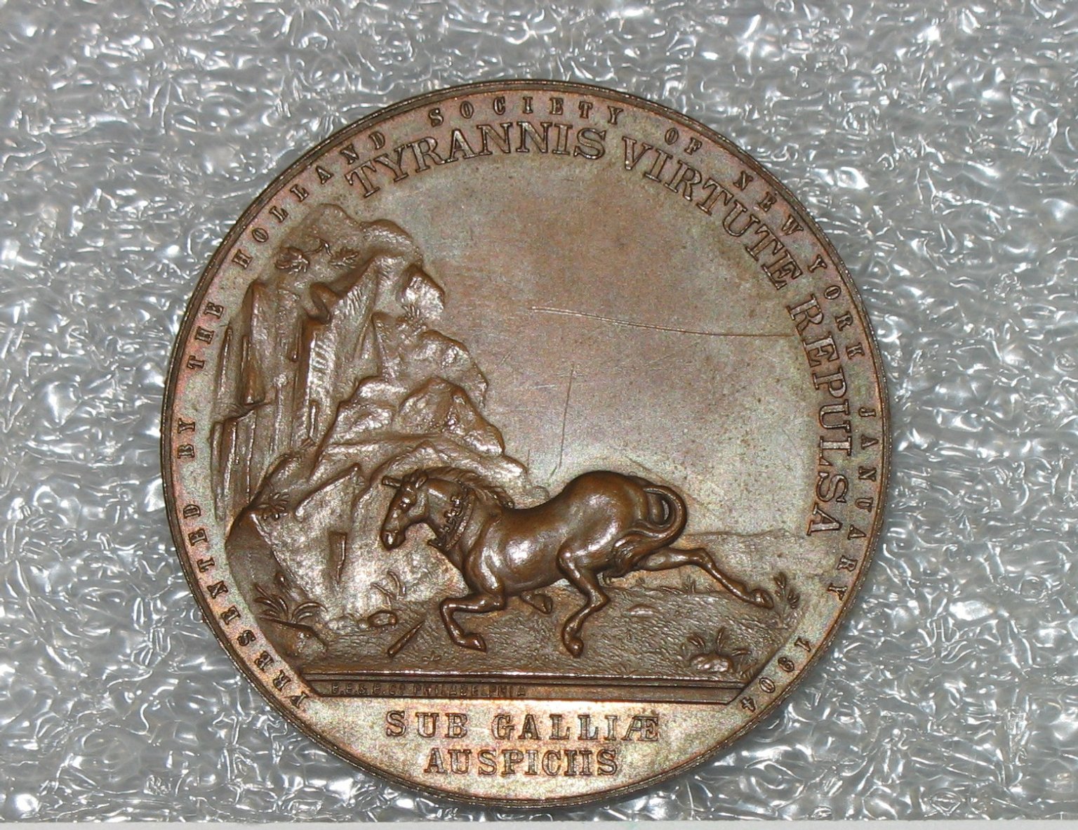 A close-up photograph of a circular gold medal featuring an embossed design.